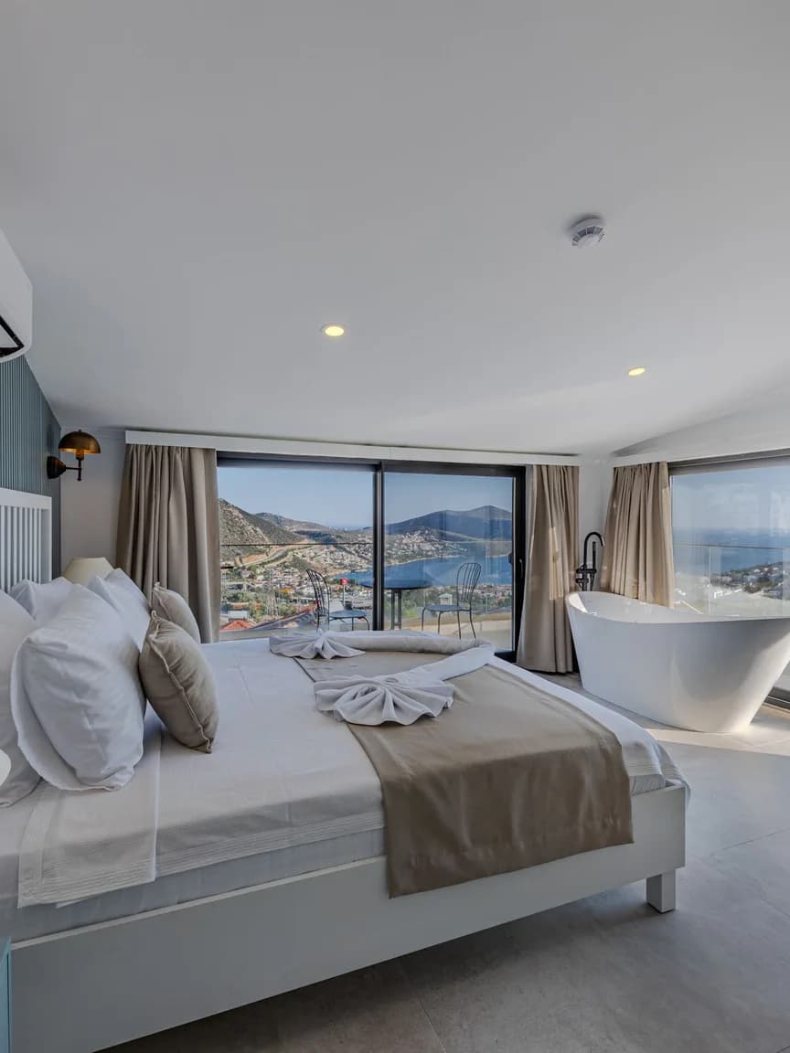 A hotel suite with a modern freestanding tub beside the bed, overlooking the sea