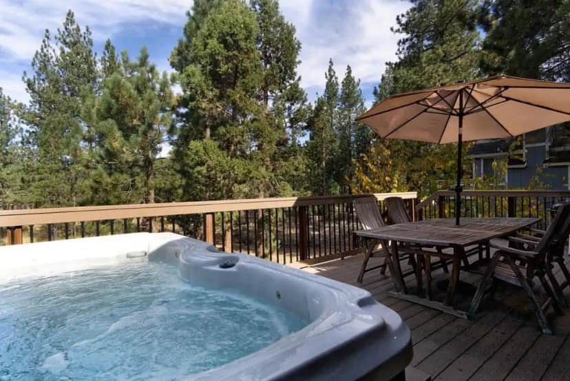 a hot tub on a deck with a table and an umbrella at All About Fun-1149 by Big Bear Vacations in Big Bear Lake