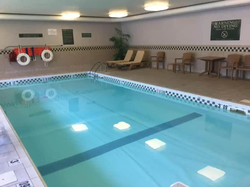 a large swimming pool in a room with chairs and tables at Baymont by Wyndham Mishawaka South Bend Area in Mishawaka