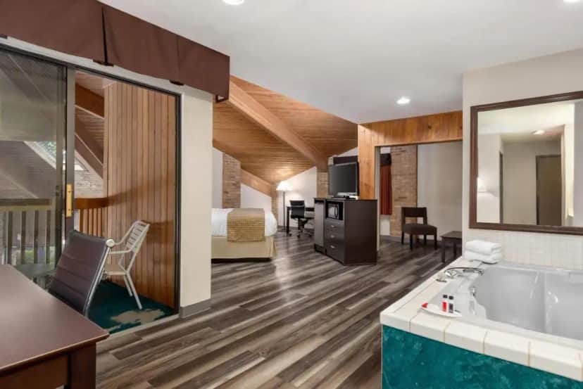 a hotel room with a tub and a bedroom at Baymont by Wyndham Monroe in Monroe
