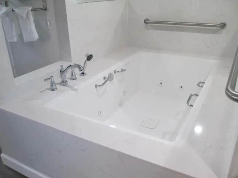 a white bathroom with a bath tub with a mirror at Claremont Lodge in Claremont