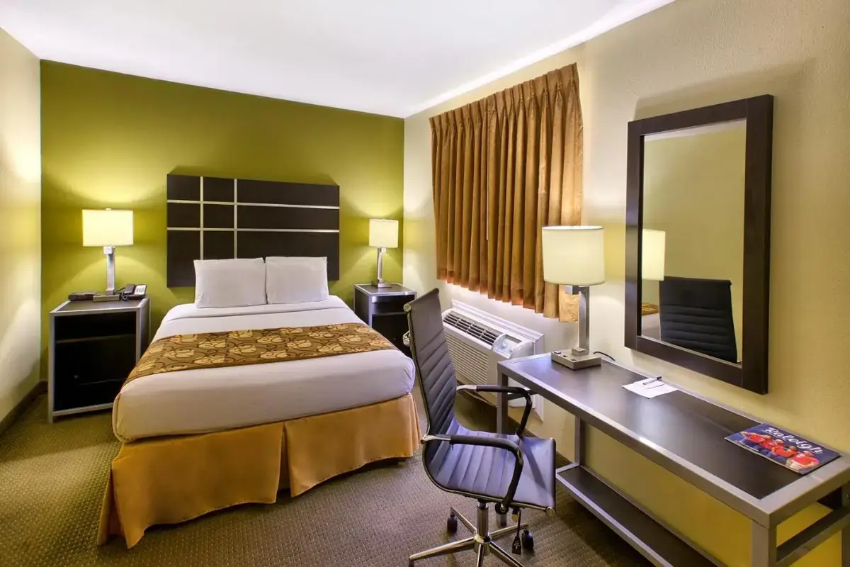 a hotel room with a bed and a desk and a mirror at Country Hearth Inn of Knightdale in Knightdale