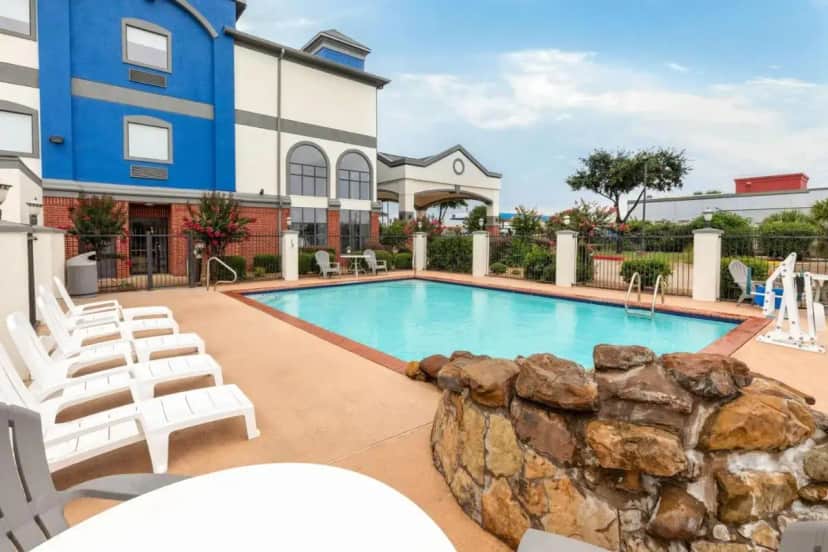 a swimming pool with white chairs and a building at Days Inn & Suites by Wyndham Sam Houston Tollway in Houston