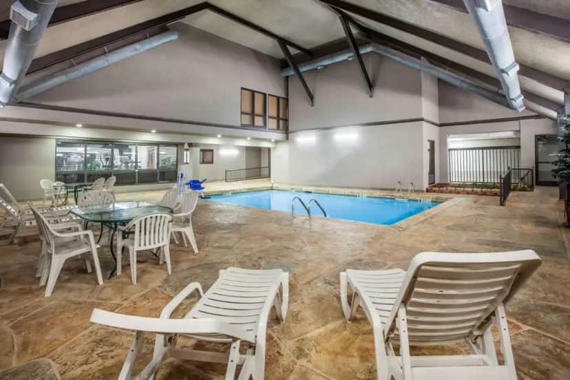 a pool with white chairs and a table and a table and a pool at Days Inn & Suites by Wyndham Tyler in Tyler