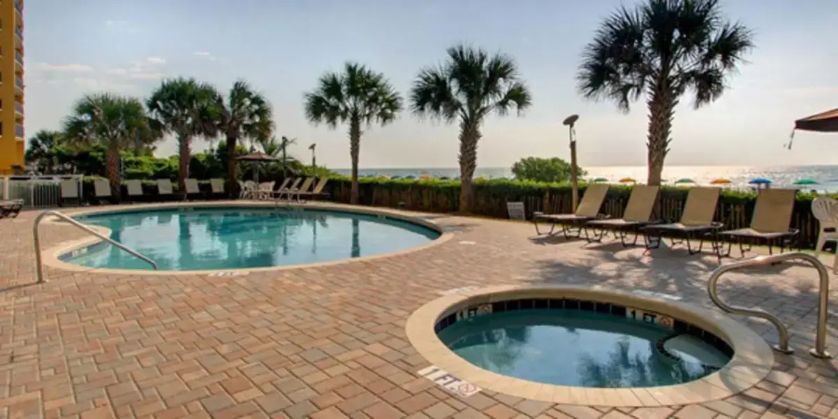 a swimming pool in a brick patio with chairs and trees at Beachfront Condo at Dunes Village Resort in Myrtle Beach