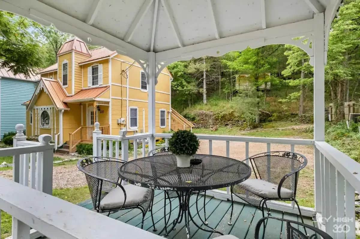 a porch with a table and chairs and a yellow house at Eureka Memories in Eureka Springs