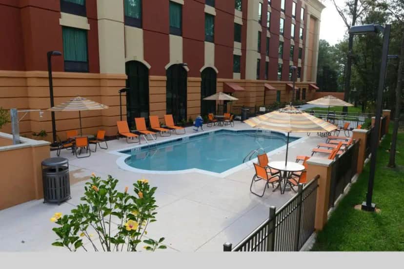 a pool with chairs and tables and umbrellas next to a building at Hampton Inn & Suites Albany at Albany Mall in Albany