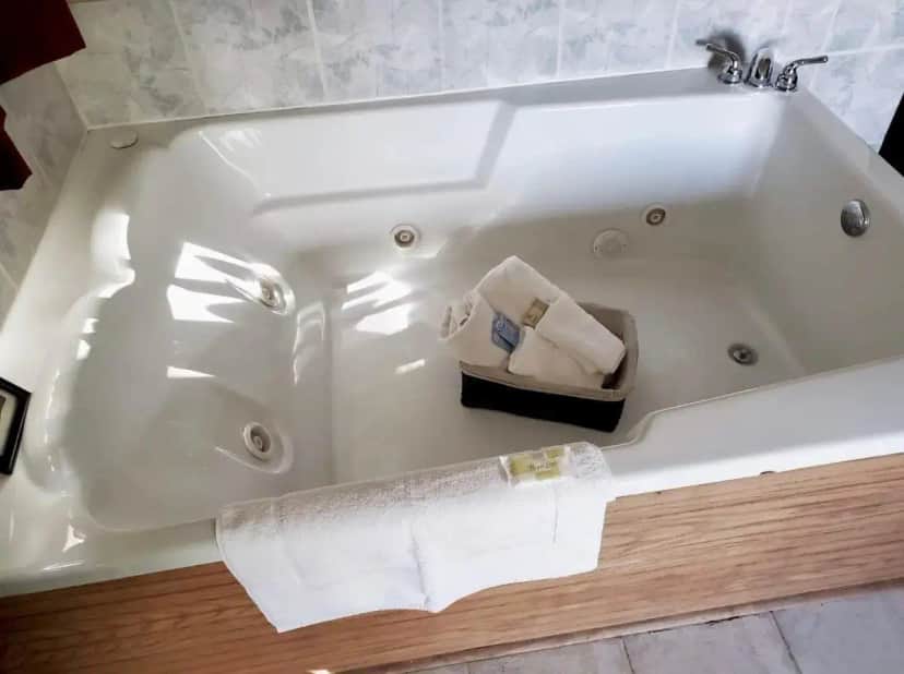 a white bath tub with towels in a bathroom at Heritage Inn Hotel in Watertown