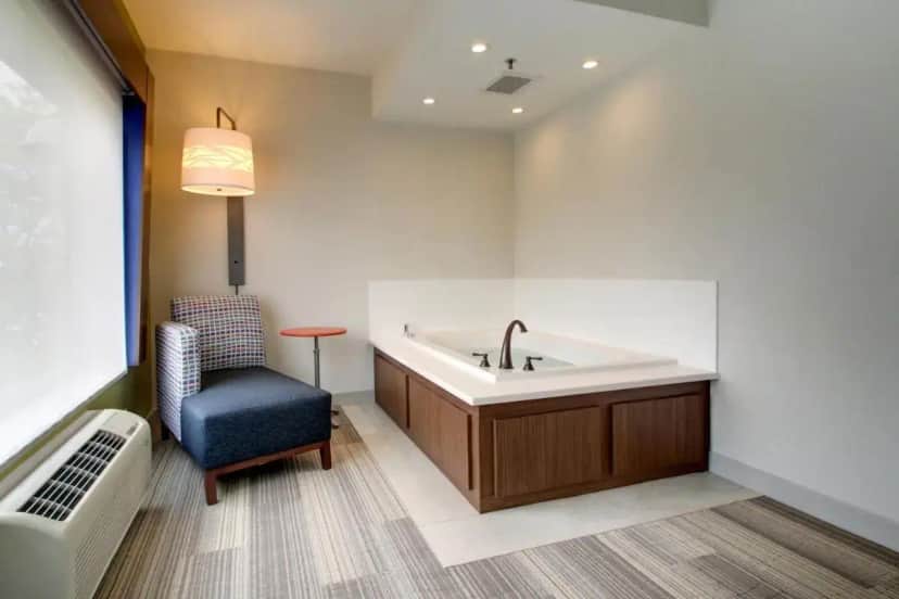 a bathroom with a bath tub and a chair at Holiday Inn Express & Suites Aurora - Naperville by IHG in Aurora