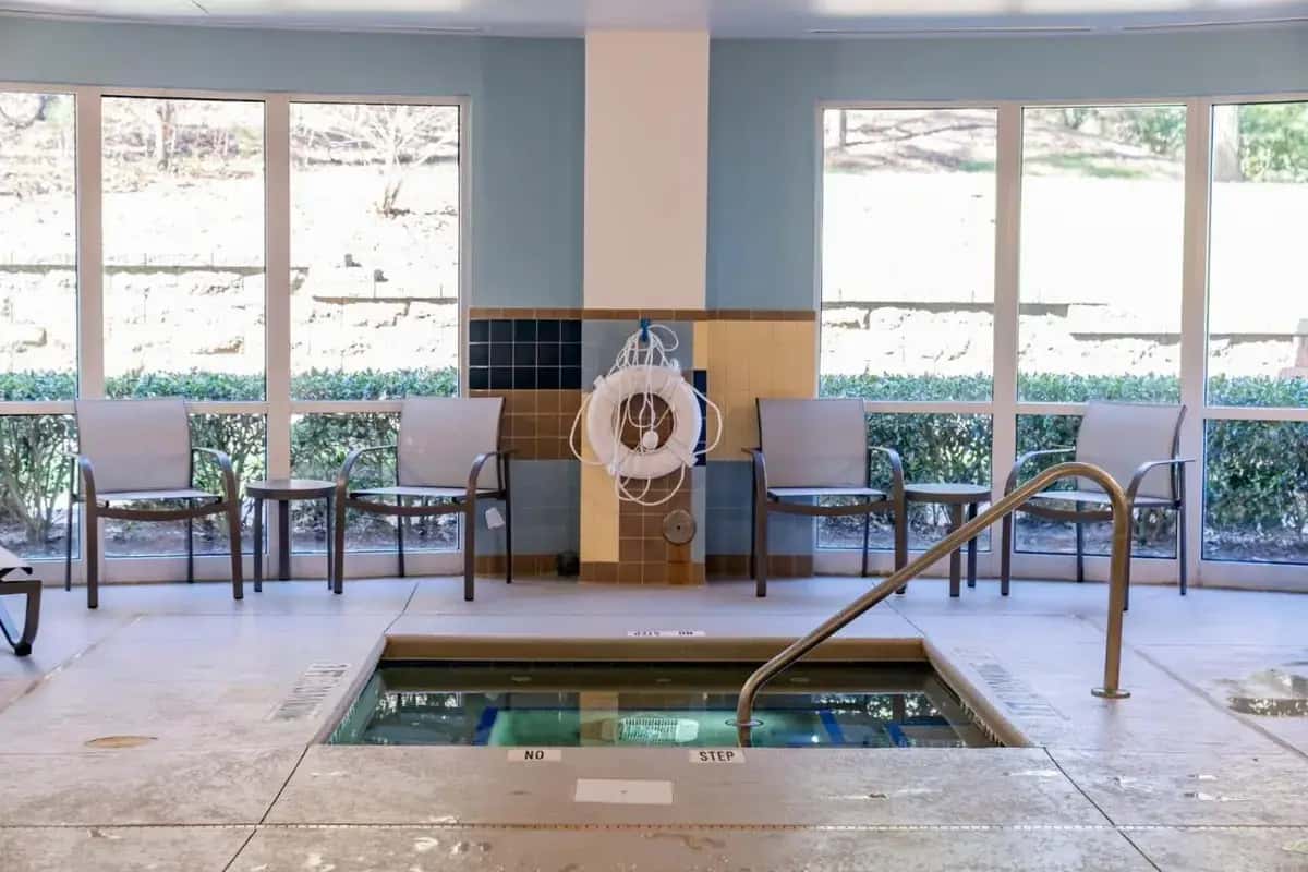 a room with a hot tub and chairs and windows at Holiday Inn Express Hotel Raleigh Southwest by IHG in Raleigh
