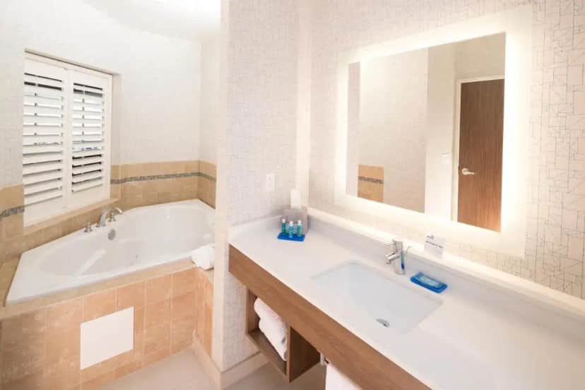 a bathroom with a tub and a sink and a mirror at Holiday Inn Express Hotel & Suites Bay City by IHG in Bay City