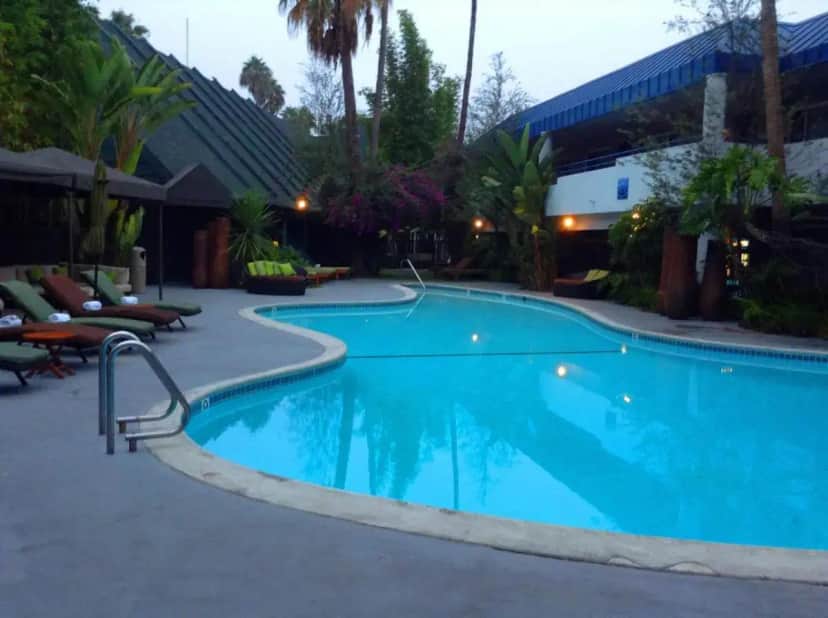 a large blue swimming pool with chairs and a building at Hotel Current in Long Beach