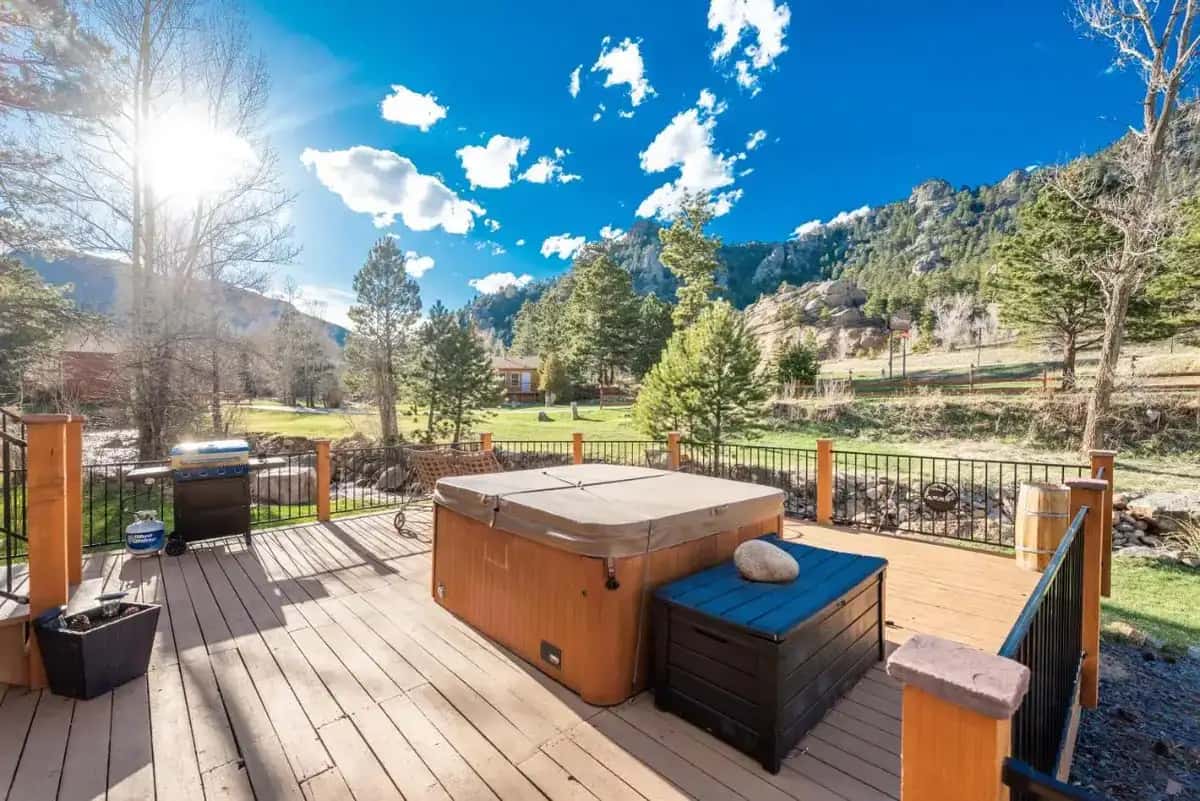 a hot tub on a wooden deck with mountains in the background at 4 Seasons Inn on Fall River in Estes Park