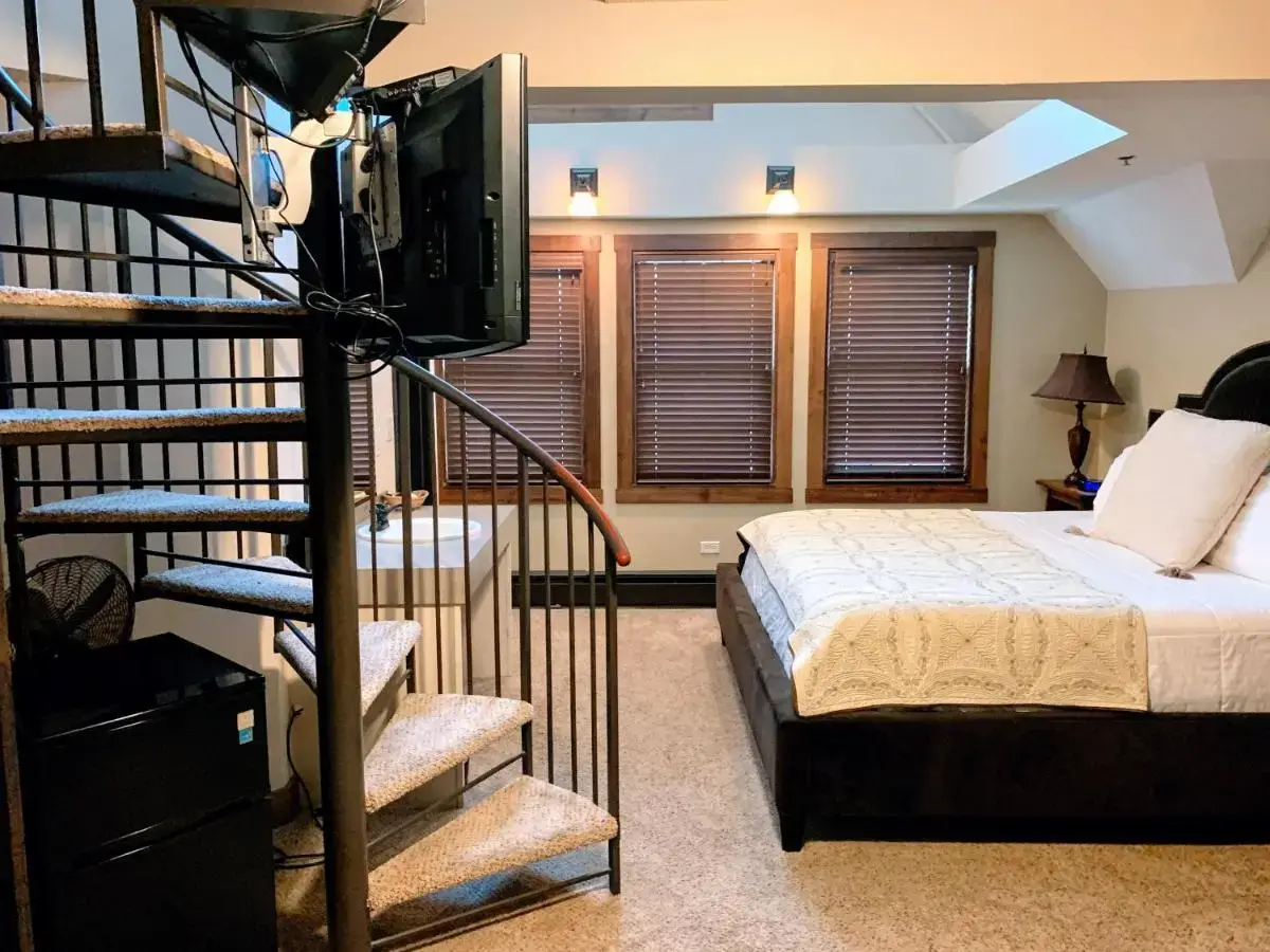 a bedroom with a bed and a staircase with a television at Iowa House Historic Inn in Ames