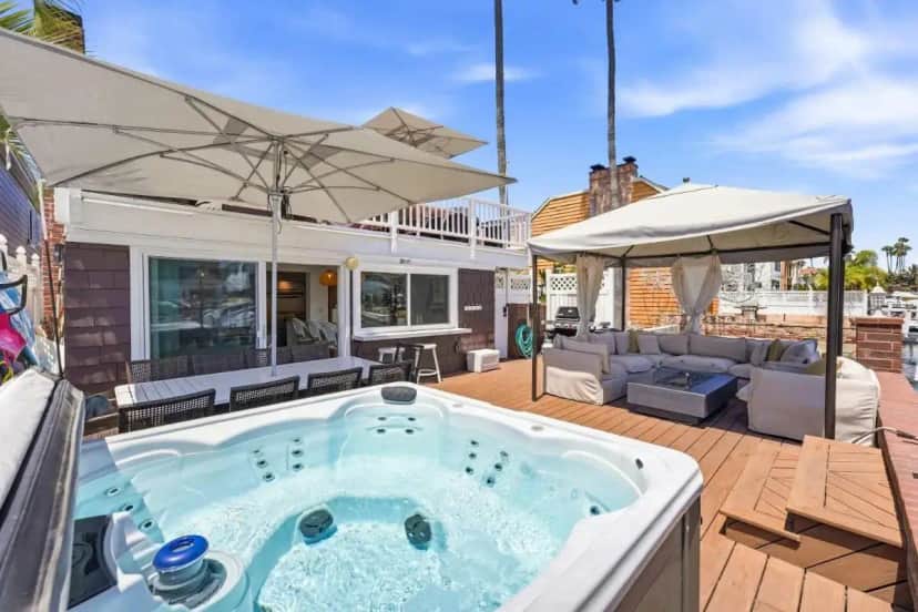 a hot tub on a deck with an umbrella at Magical BayFRONT Home with Epic Dock and Hot Tub in Newport Beach