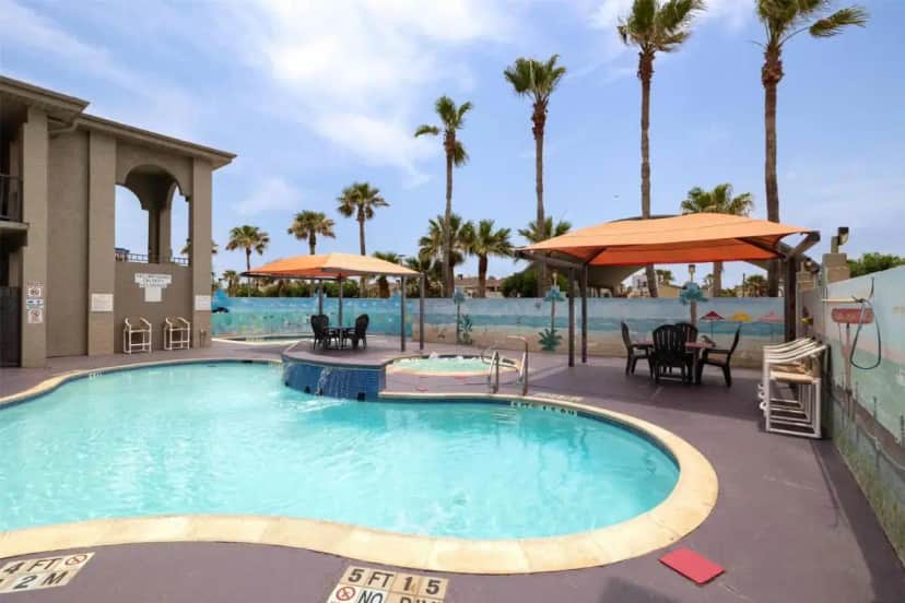 a pool at a resort with chairs and umbrellas at Ramada by Wyndham & Suites South Padre Island At the Beach in South Padre Island