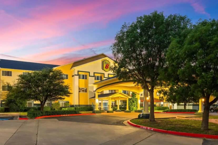 a hotel with a yellow building with trees in front at Super 8 by Wyndham Lubbock West in Lubbock