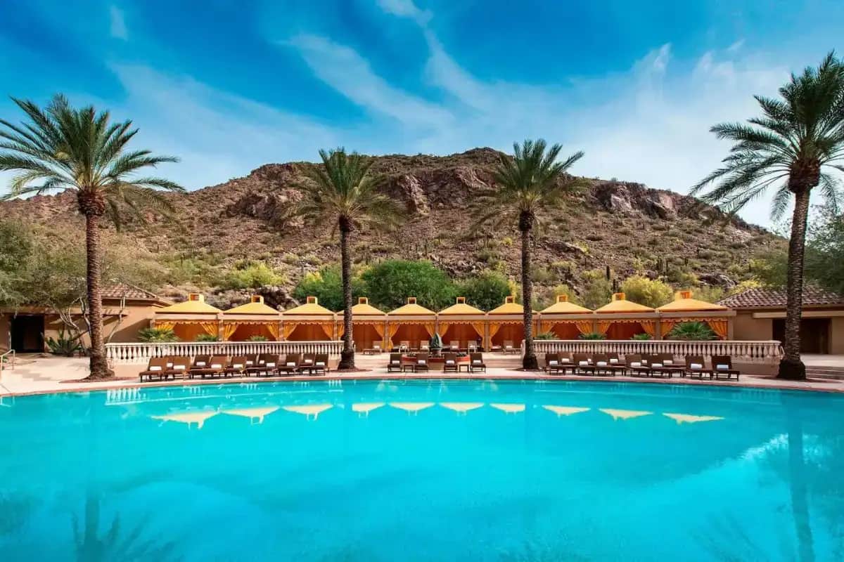 a resort pool with palm trees and mountains in the background
