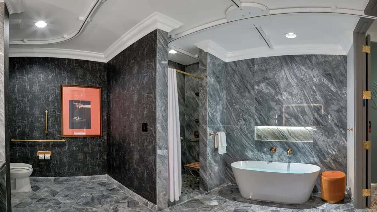 Modern bathroom with gray marble surfaces, featuring a freestanding tub, roll-in shower, separate toilet with grab bars, and a mobility lift track in the ceiling going to the toilet, shower, and tub.