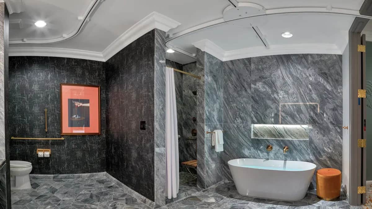 Modern bathroom with gray marble surfaces, featuring a freestanding tub, roll-in shower, separate toilet with grab bars, and a mobility lift track in the ceiling going to the toilet, shower, and tub.