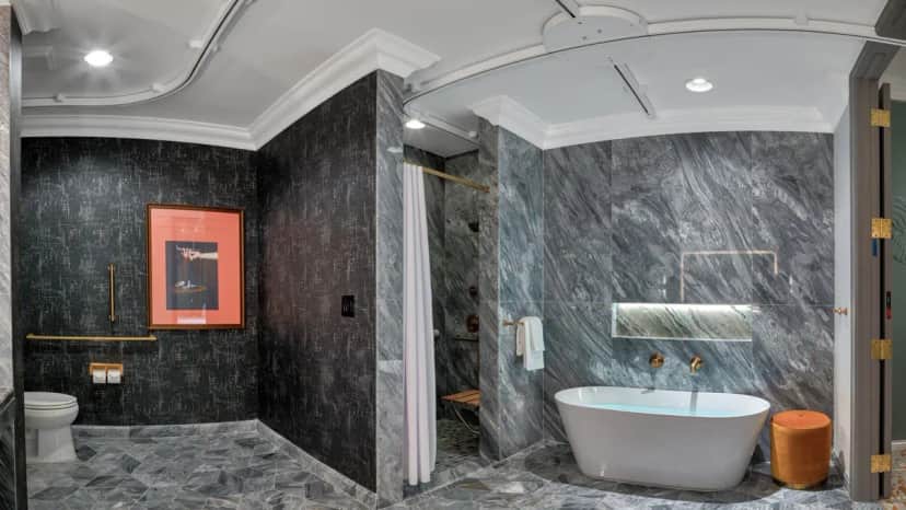 Modern bathroom with gray marble surfaces, featuring a freestanding tub, roll-in shower, separate toilet with grab bars, and a mobility lift track in the ceiling going to the toilet, shower, and tub.