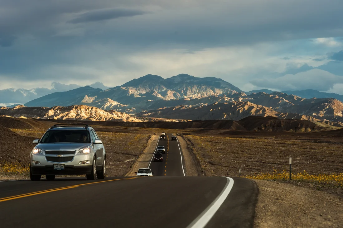 Cars on Badwater Road beneath desert mountains in Death Valley National Park