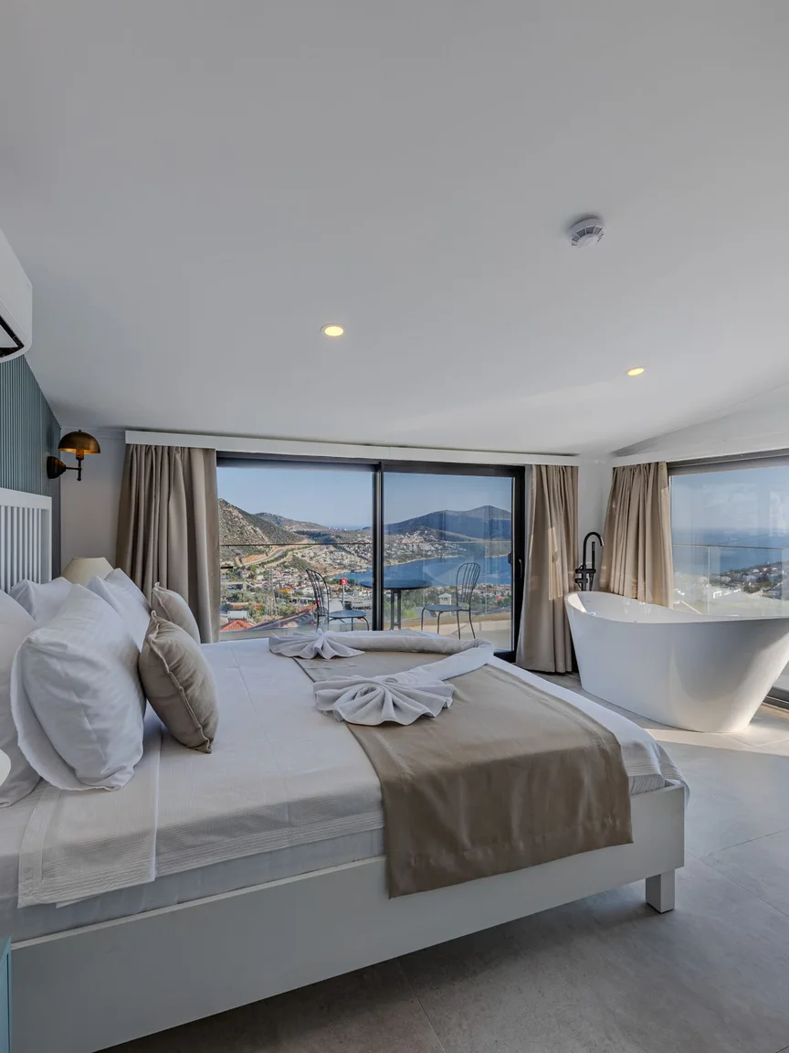 A hotel suite with a modern freestanding tub beside the bed, overlooking the sea